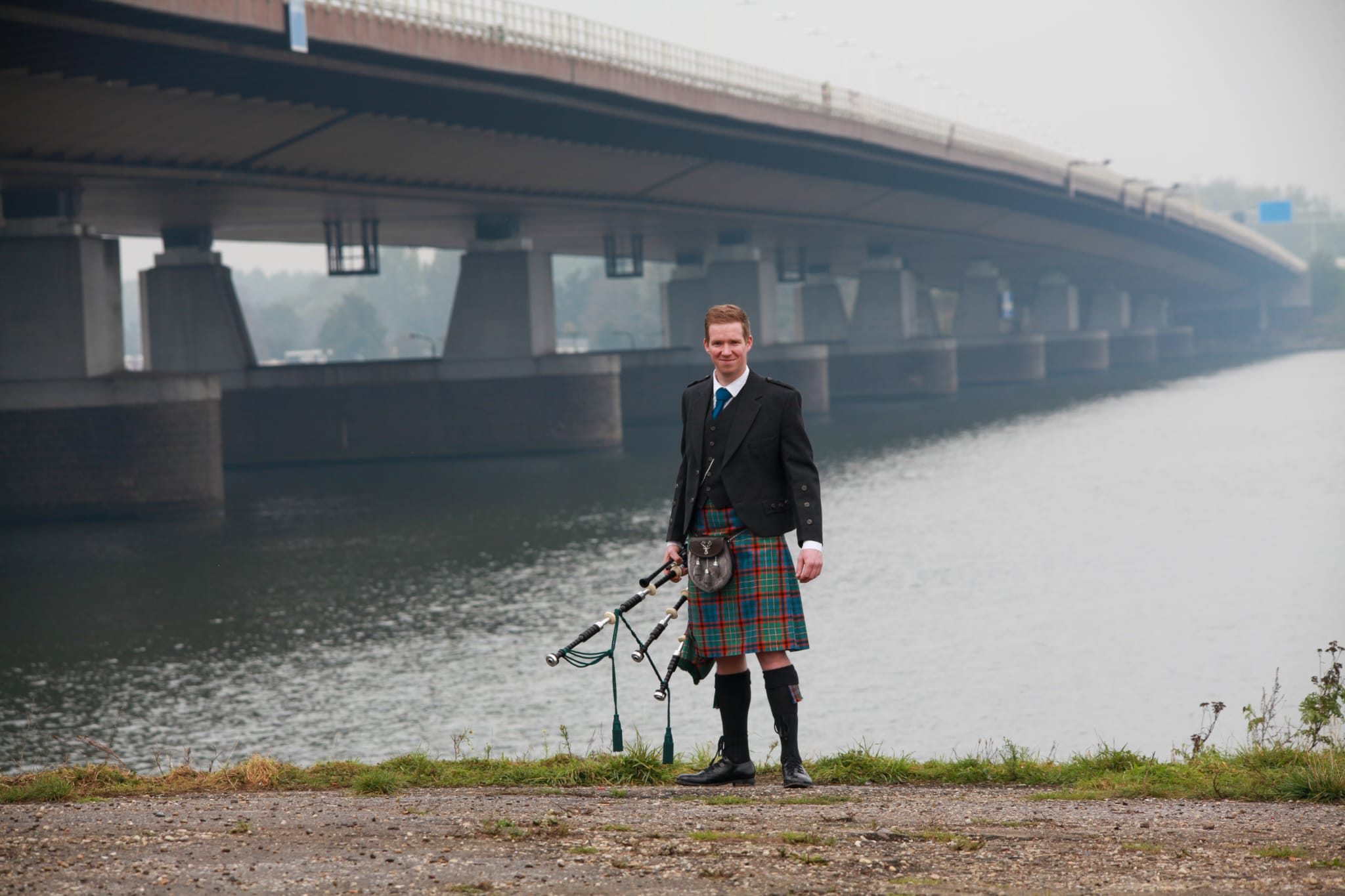 Doedelzakspeler in kilt op de oever bij de brug over de rivier